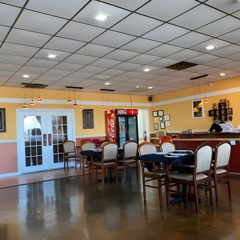 Restaurant interior with yellow walls, white double doors, set tables, a Coca-Cola fridge, and a host stand.