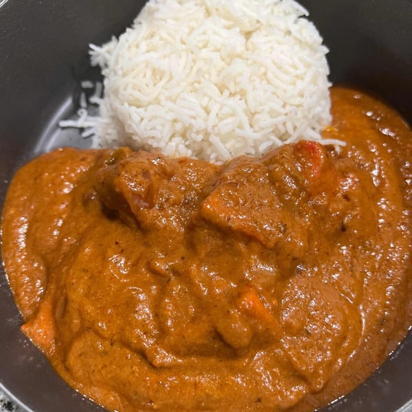 A close-up of Spice Rack's Indian butter chicken with white rice in a dark bowl.