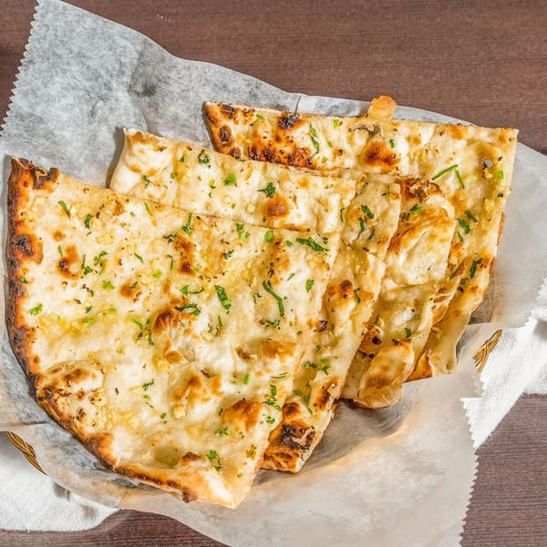 Golden brown garlic naan bread, garnished with herbs, served in a basket lined with white paper.