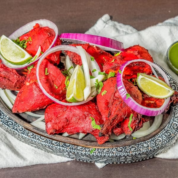 Bright red Indian chicken tikka, garnished with lime wedges, red and white onion rings, and cilantro.