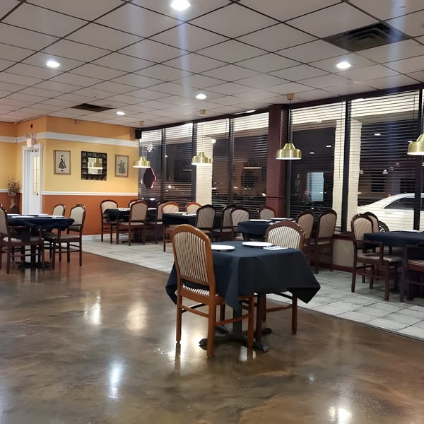 Empty restaurant dining room with tables set with dark tablecloths and chairs, illuminated by overhead lights.