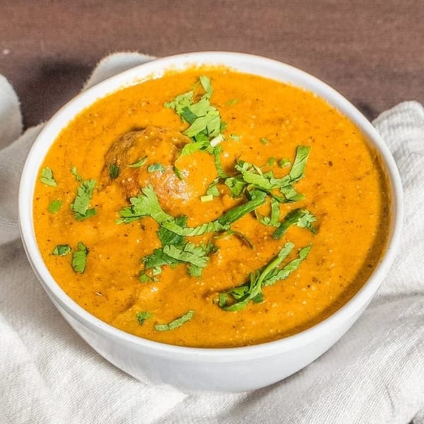 A white bowl of orange Indian curry, garnished with fresh green cilantro, on a white cloth.