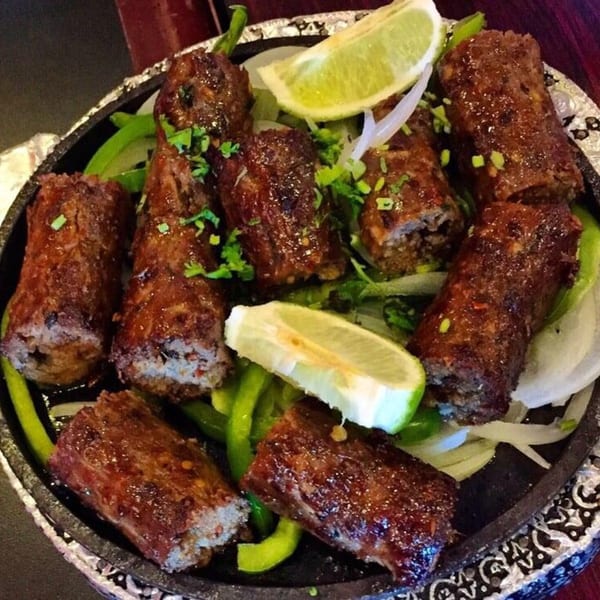 Indian seekh kebabs, garnished with lime wedges, green peppers, and onions, served on a hot platter.